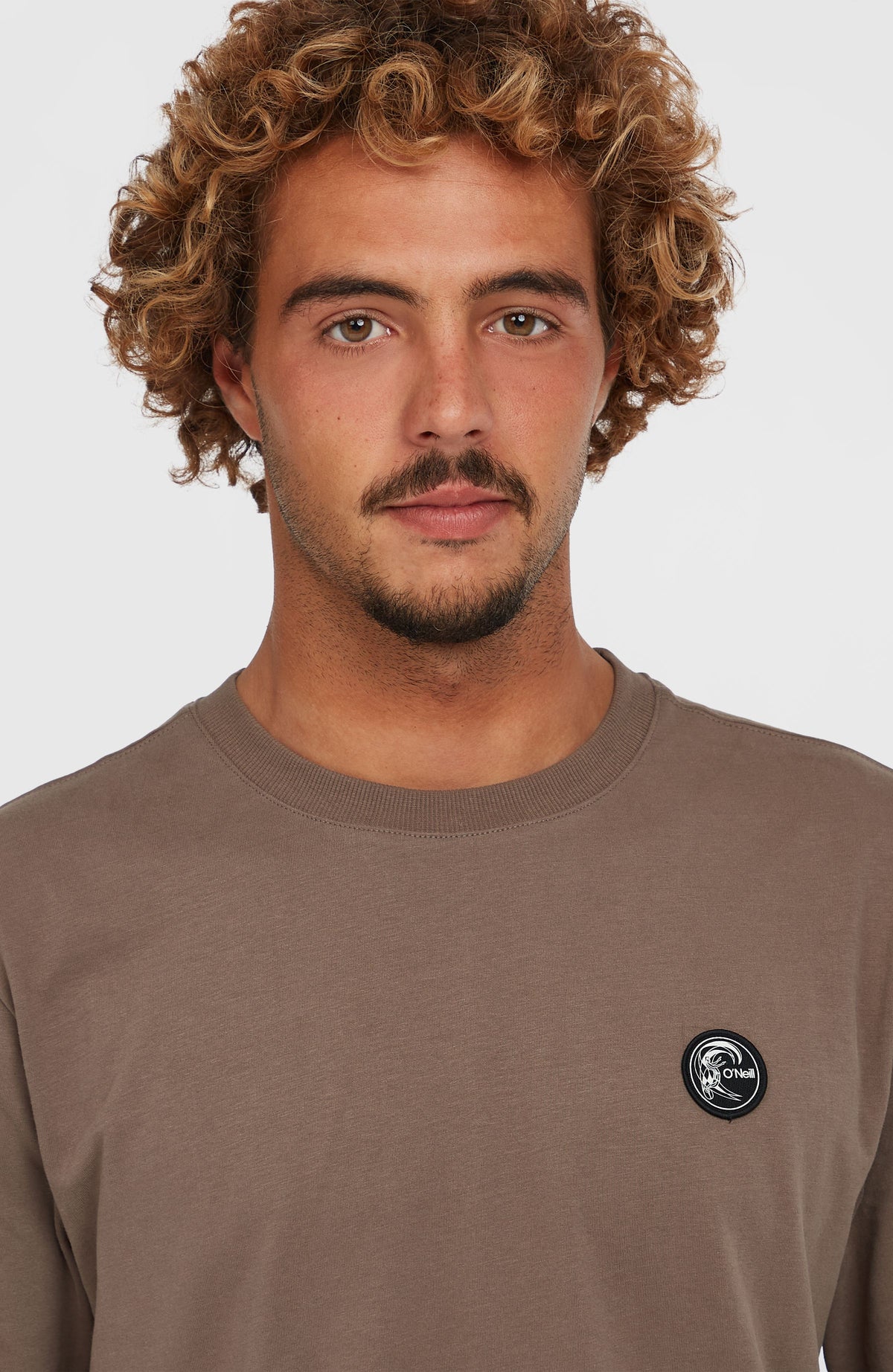Nahaufnahme von Rundhalsausschnitt und Logo-Badge am braunen O'Riginals Badge T-Shirt