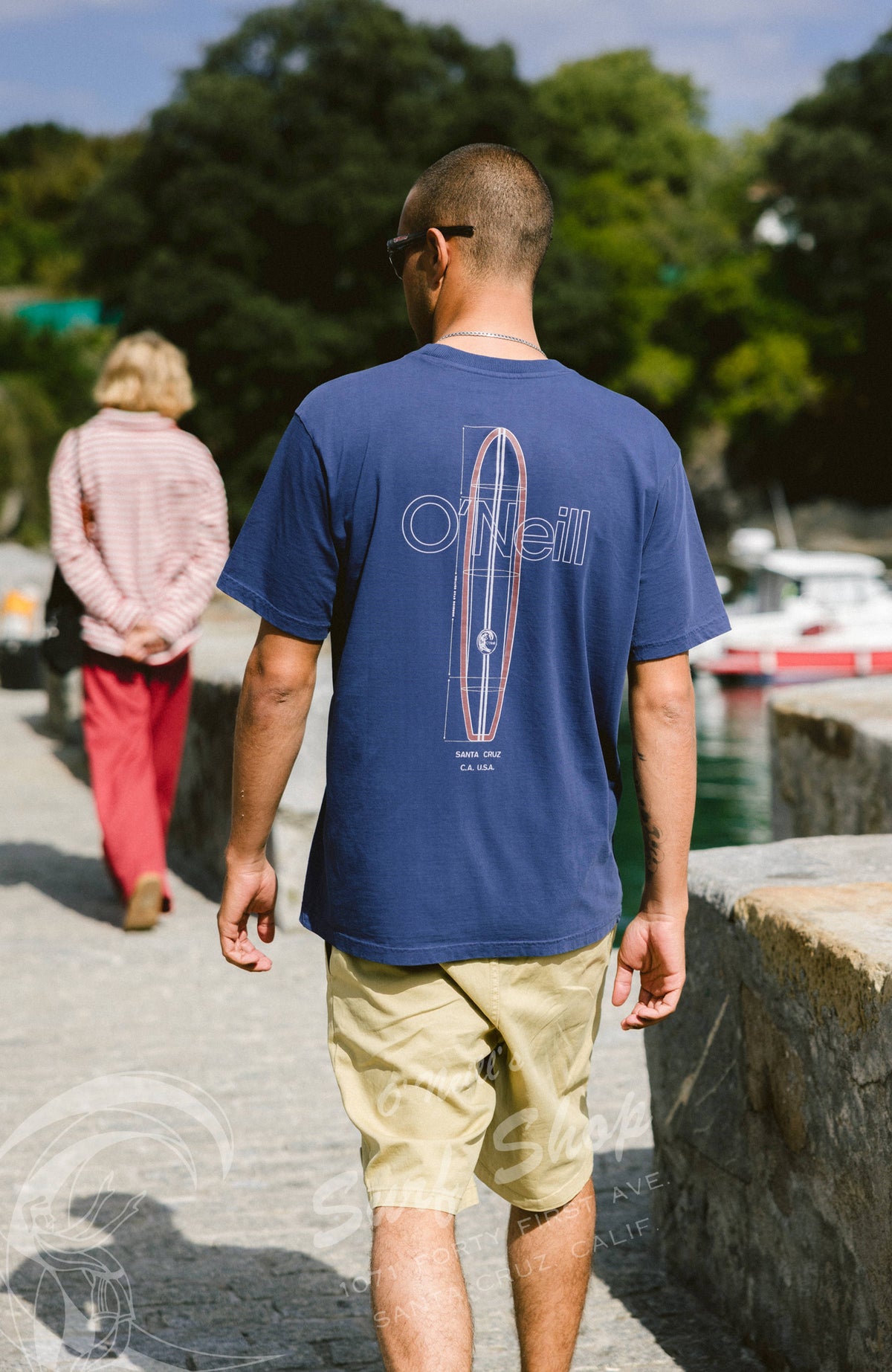 O'Riginals Vintage Graphic T-Shirt in Blau mit Surfboard-Print in Weiß und Rot, Rückansicht am Model am Hafen