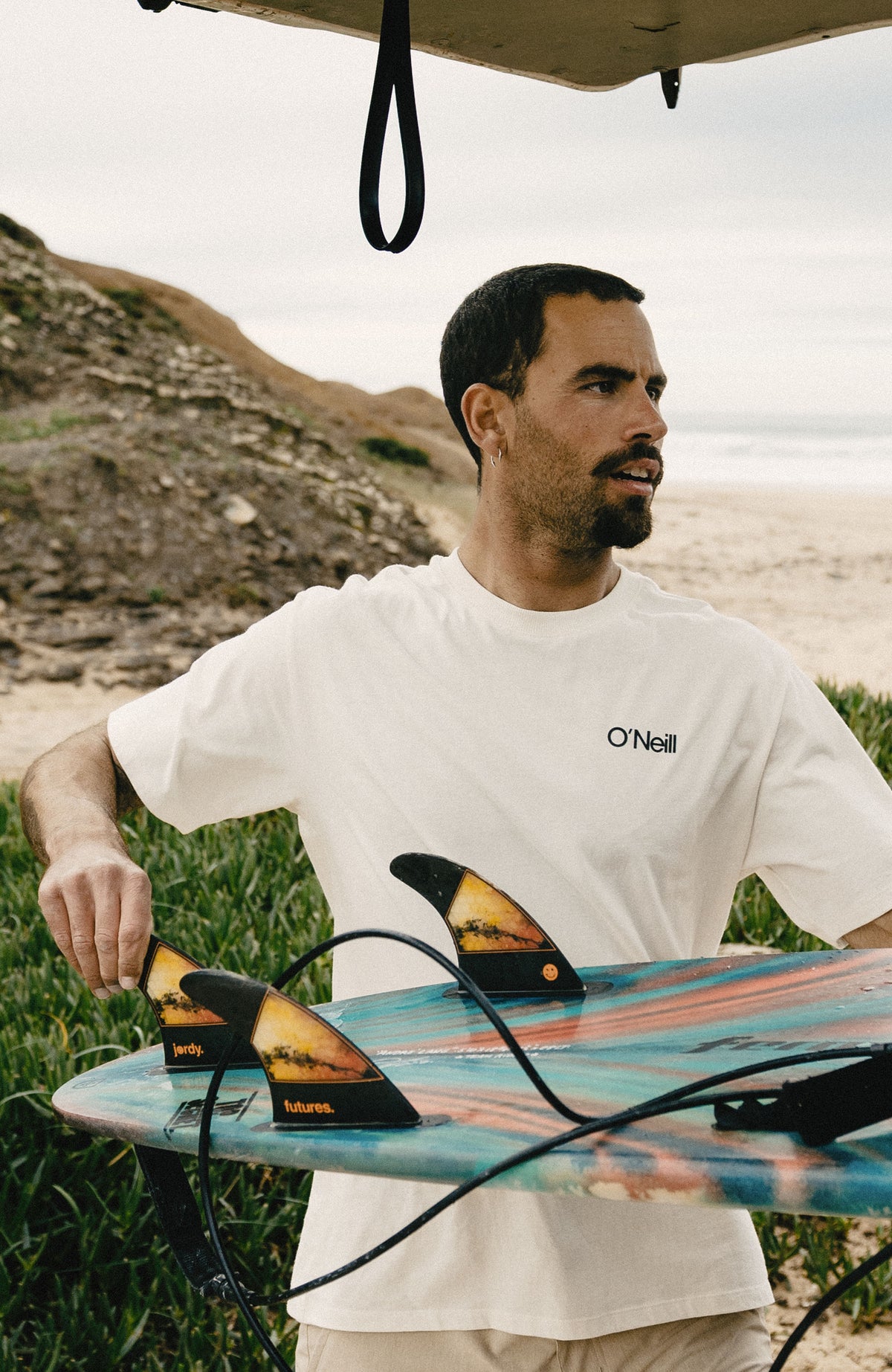 Polygiene Cotton Graphic T-Shirt für Herren, weiß mit Logo-Print in Schwarz, am Strand mit Surfbrett getragen