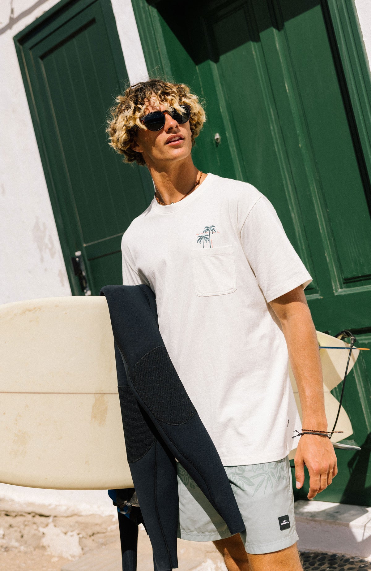 Chest Pocket T-Shirt für Herren, weiß mit Palmen-Print in Grün, getragen am Model vor einem Gebäude