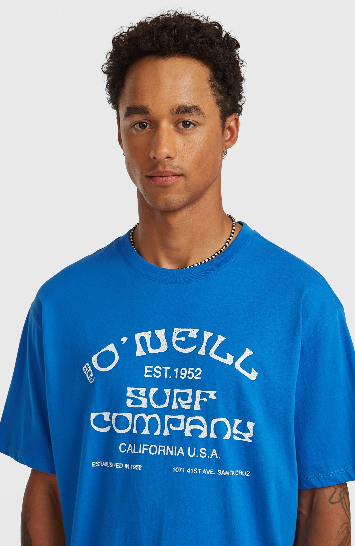 Nahaufnahme von Rundhalsausschnitt und Logo-Print des blauen Muir T-Shirt am Model
