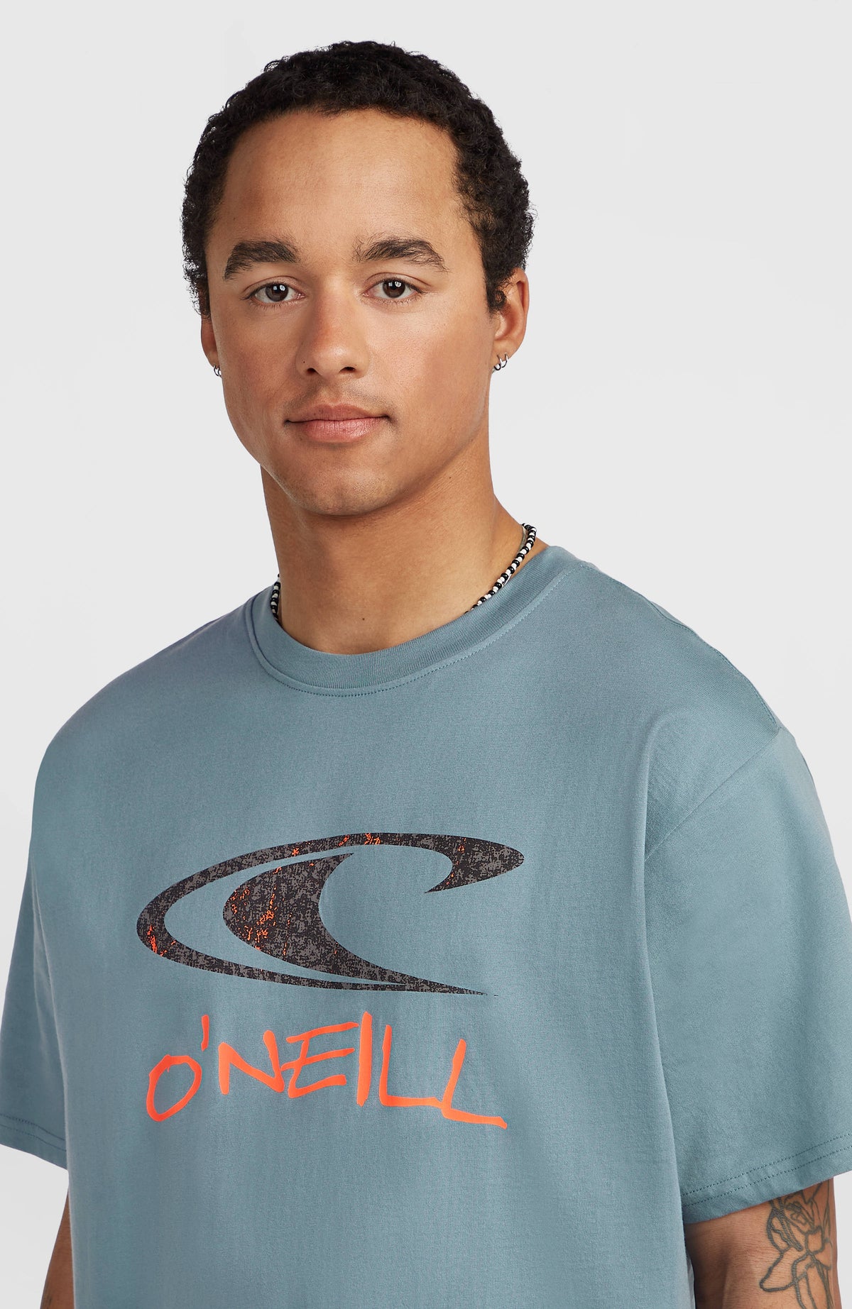 Must-Have Graphic T-Shirt, blau mit Logo-Print in Schwarz und Orange, Nahaufnahme des Rundhalsausschnitts am Model
