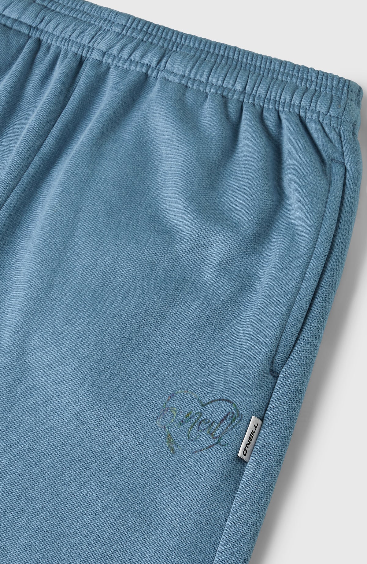 Nahaufnahme der blauen Essentials Jogginghose für Mädchen, elastischer Bund mit Eingrifftasche und Herz-Print