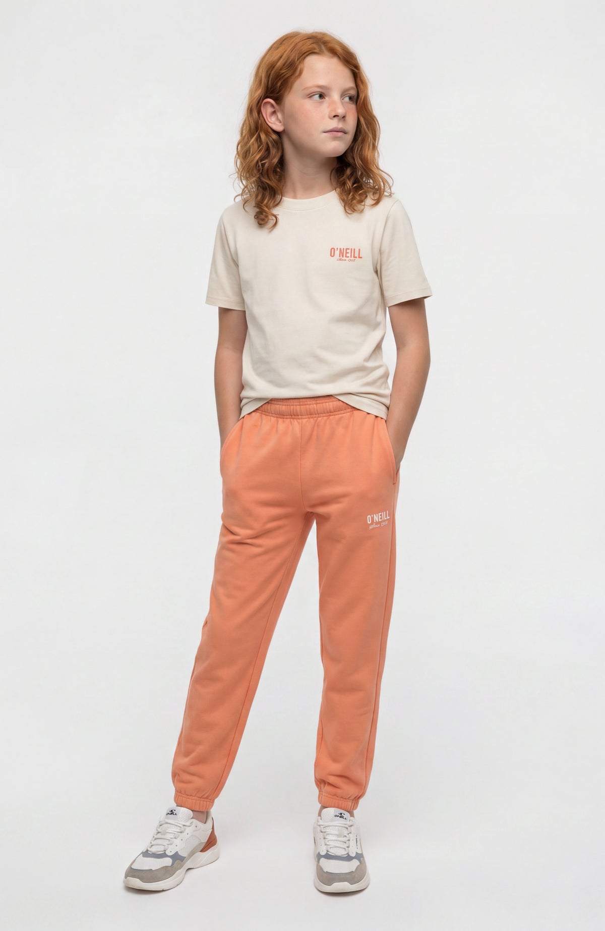 Essentials Jogginghose für Mädchen, orange mit Logo-Print in Weiß, Ganzkörperansicht getragen am Model
