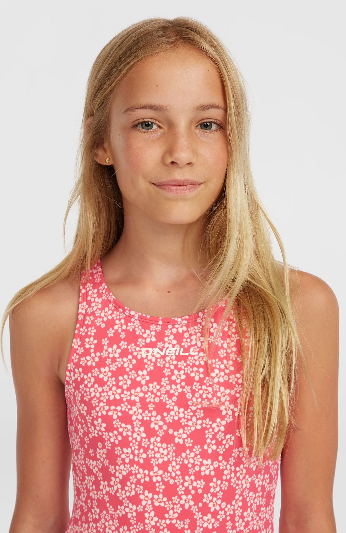 Essentials Badeanzug für Mädchen, pink mit Blumenmuster in Weiß, Nahaufnahme am Model mit Logo-Schriftzug