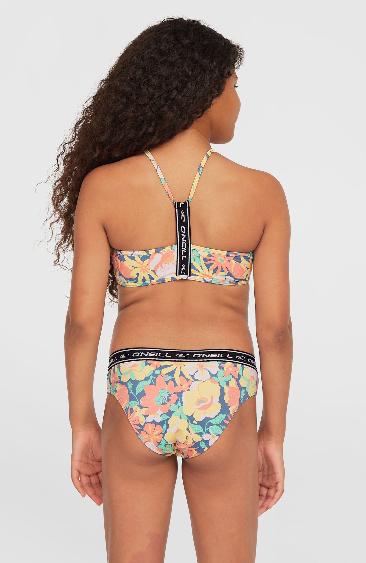 Sportclub Bikini-Set für Mädchen, blau mit Blumenmuster in Gelb und Rosa, Rückansicht mit Logo-Träger am Model