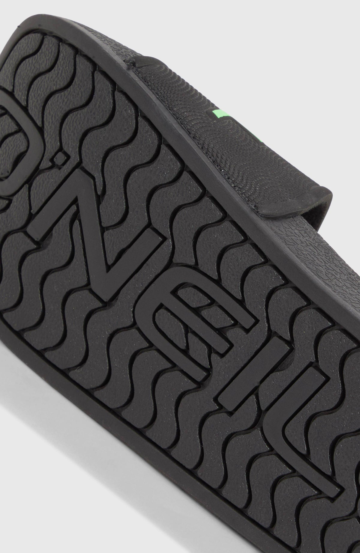 Schwarze Logo Slides für Jungen, Nahaufnahme der profilierten Laufsohle mit Wellenstruktur