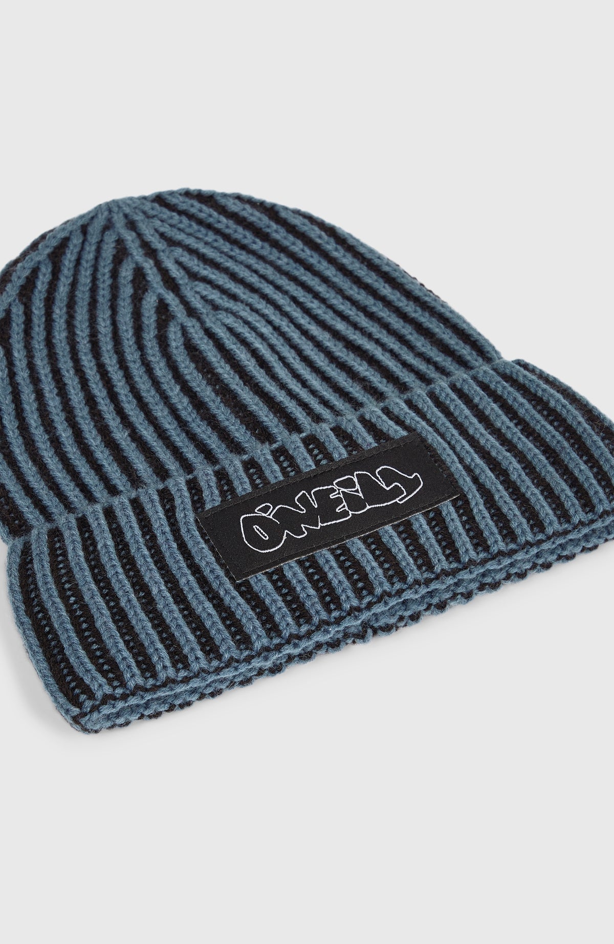 Beanie für Jungen, schwarz mit Streifenmuster in Blau, Nahaufnahme von schräg oben mit Logo-Patch