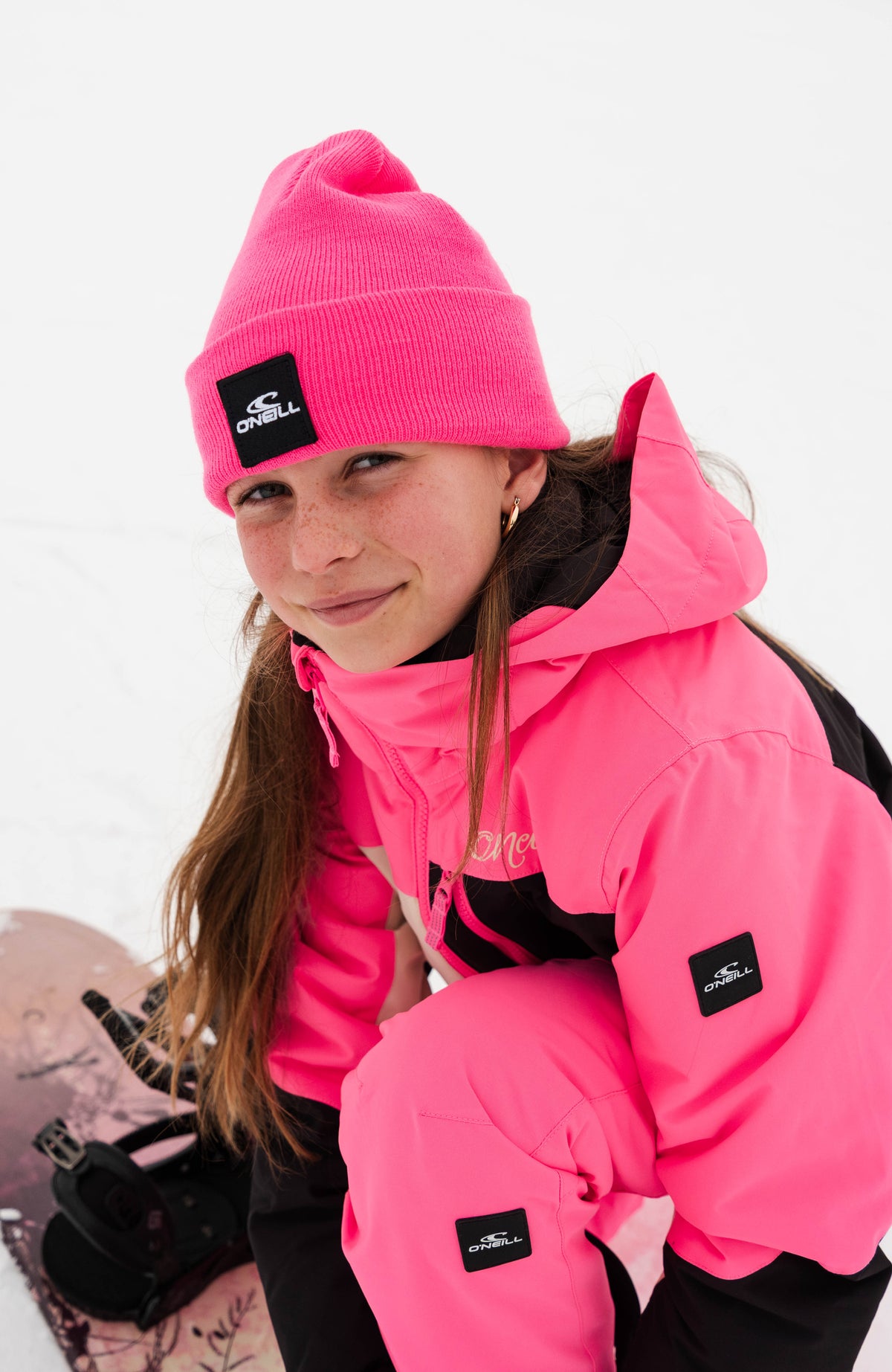 Snow Beanie für Kinder, pink, getragen am Model im Schnee, schräge Vorderansicht mit Snowboard