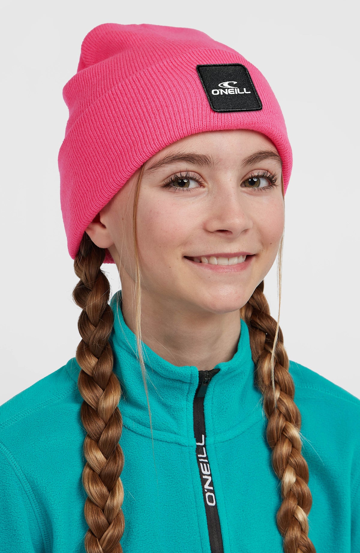 Snow Beanie für Kinder, pink, getragen am Model, Nahaufnahme von vorne mit Logo-Patch auf dem Umschlag
