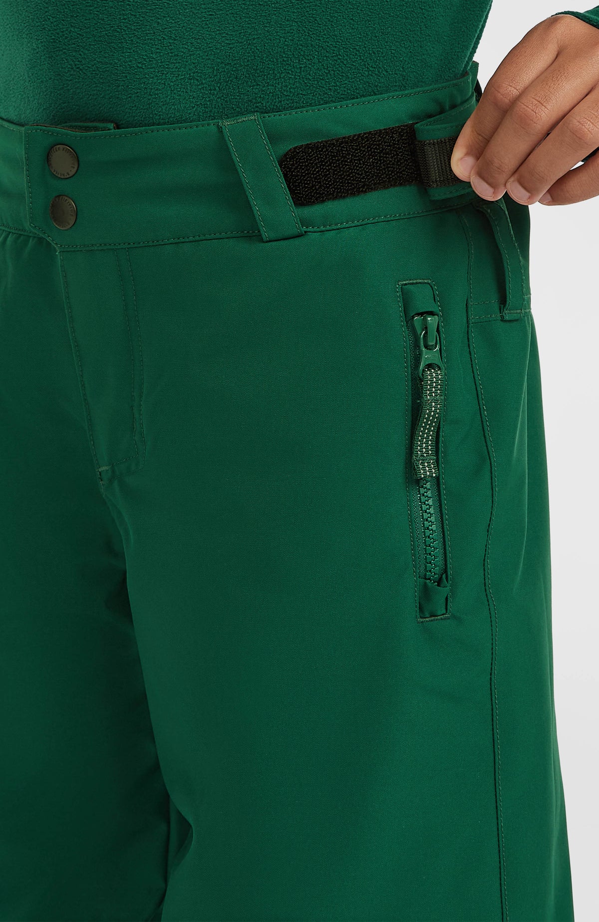 Nahaufnahme der grünen FWC'Cruz Skihose am Model mit Reißverschlusstasche und Klettverschluss am Bund