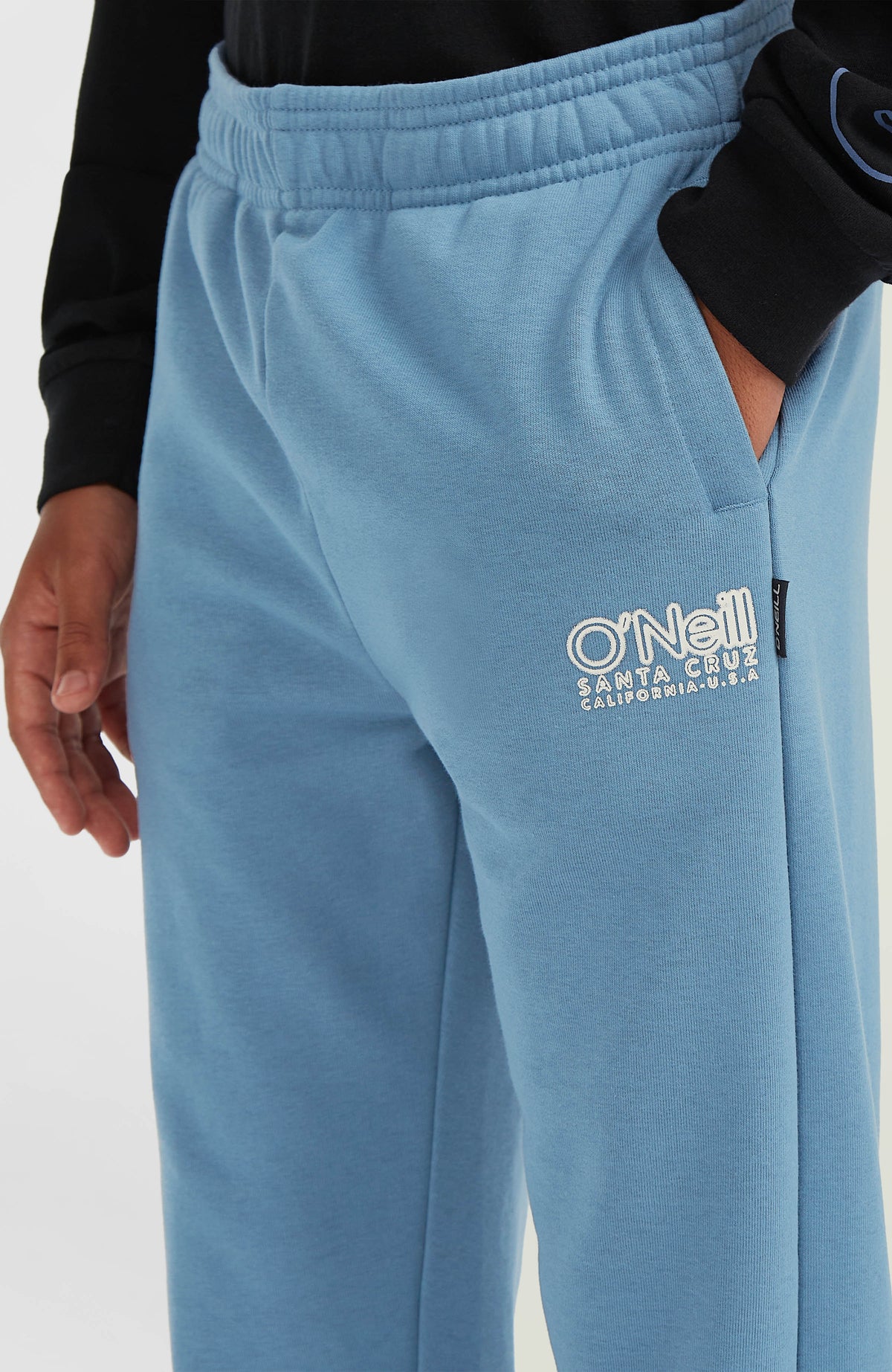 Essentials Jogginghose in Blau, Nahaufnahme am Model mit weißer Logo-Stickerei an der Seitentasche