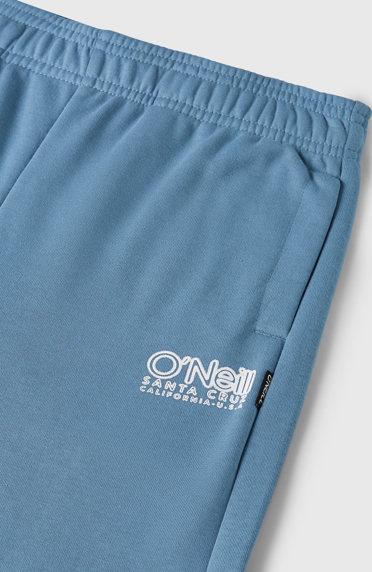 Nahaufnahme der blauen Essentials Jogginghose, elastischer Bund und weiße Logo-Stickerei an der Tasche