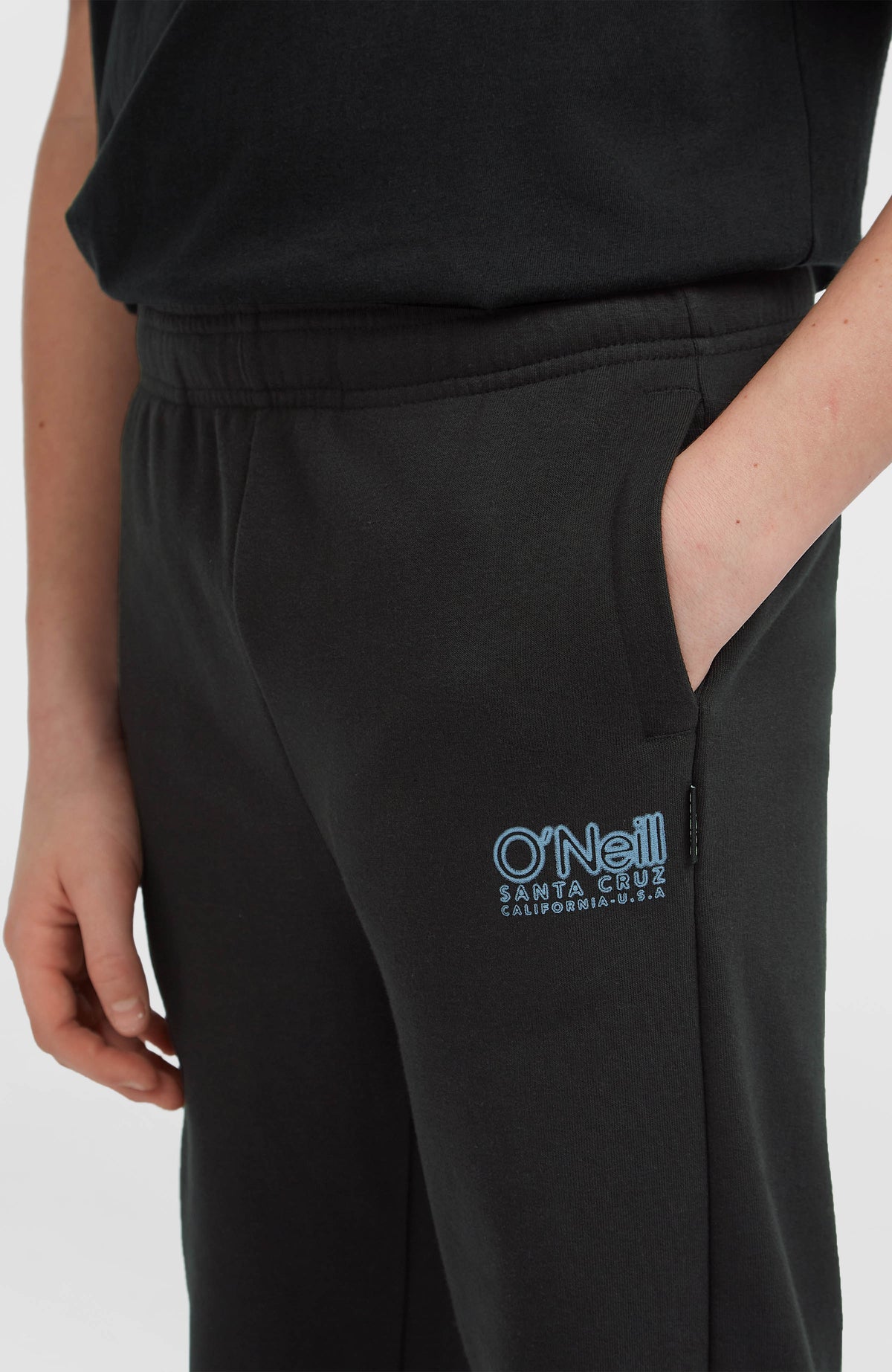 Essentials Jogginghose für Jungen, schwarz mit Logo-Print in Hellblau, Nahaufnahme der Seitentasche am Model