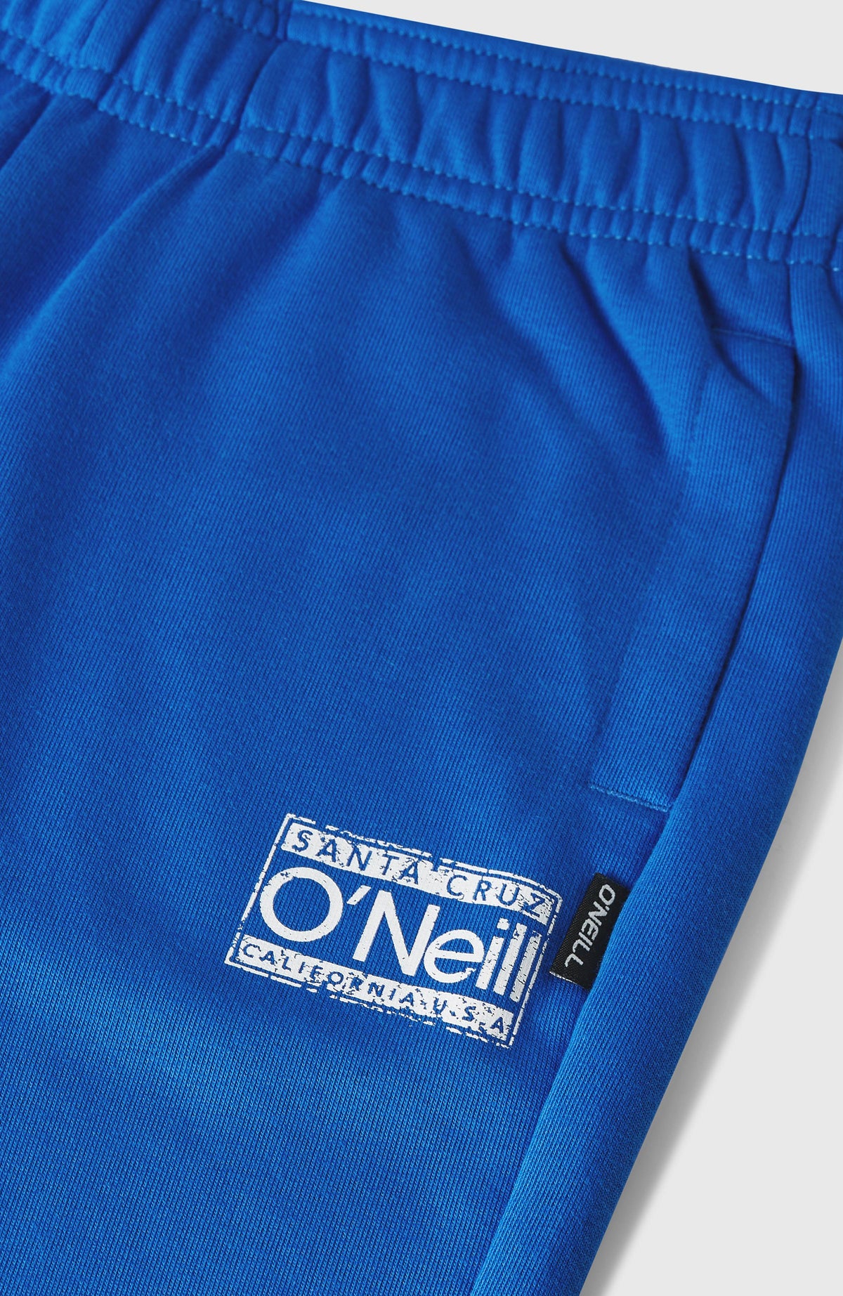Nahaufnahme des Logo-Prints an der blauen Cali Jogginghose, flach liegend