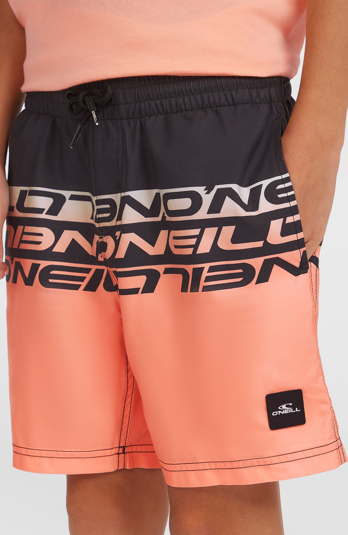 O'Neill Cali Stripe 14'' Badehose für Jungen, pink mit Logo-Print in Schwarz, Nahansicht am Model mit Logo-Patch