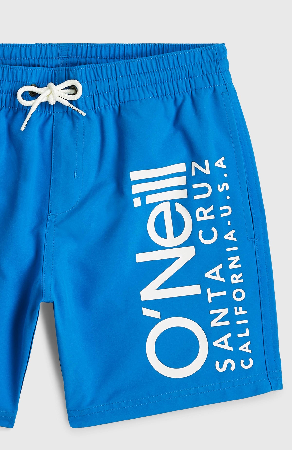 Nahaufnahme der blauen Cali Badehose für Jungen mit weißem Logo-Print am Hosenbein, flach liegend