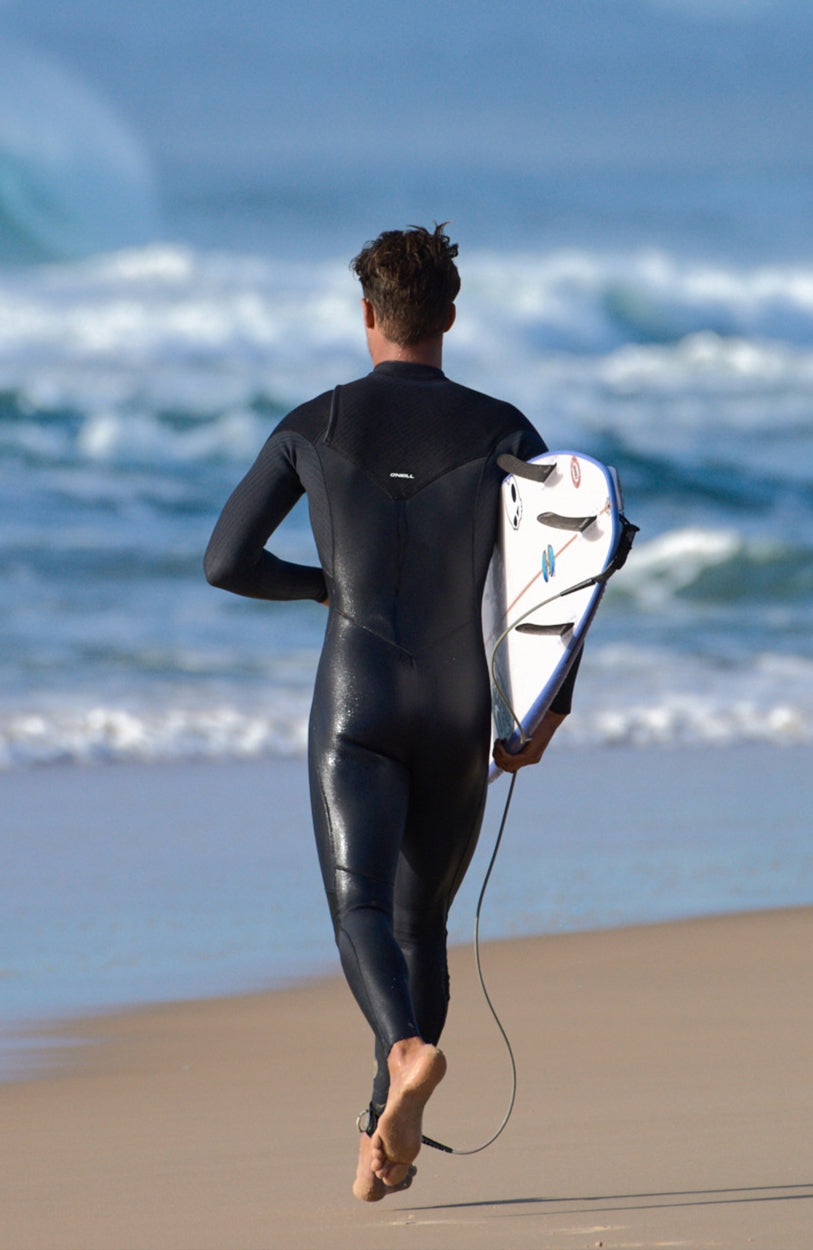 Schwarzer Hyperfreak Plus Neoprenanzug für Herren, am Strand mit Surfboard, Rückansicht