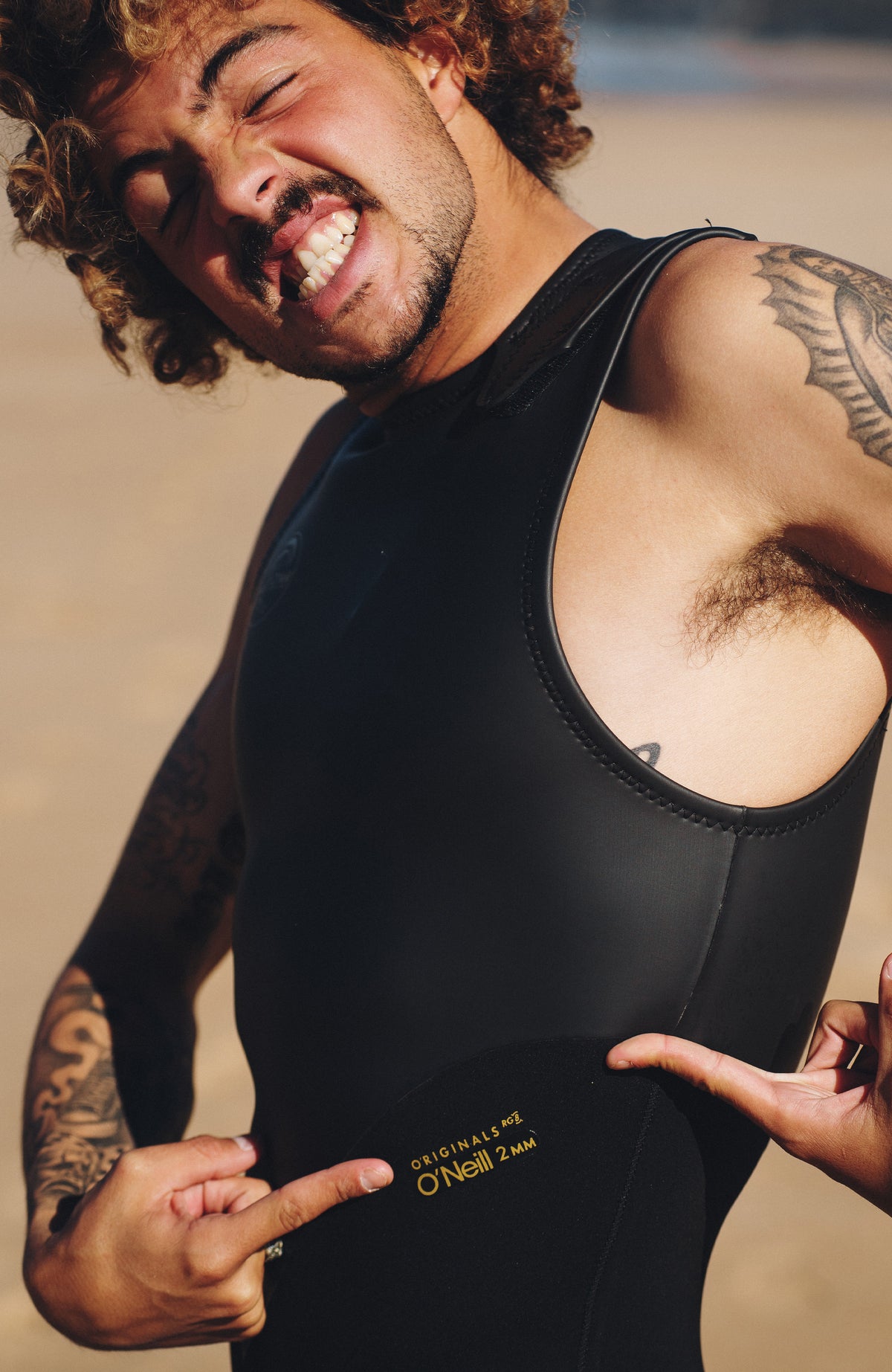 O'Riginals 2mm Long John Wetsuit Neoprenanzug, schwarz, am Strand, Nahaufnahme des seitlichen Logo-Prints