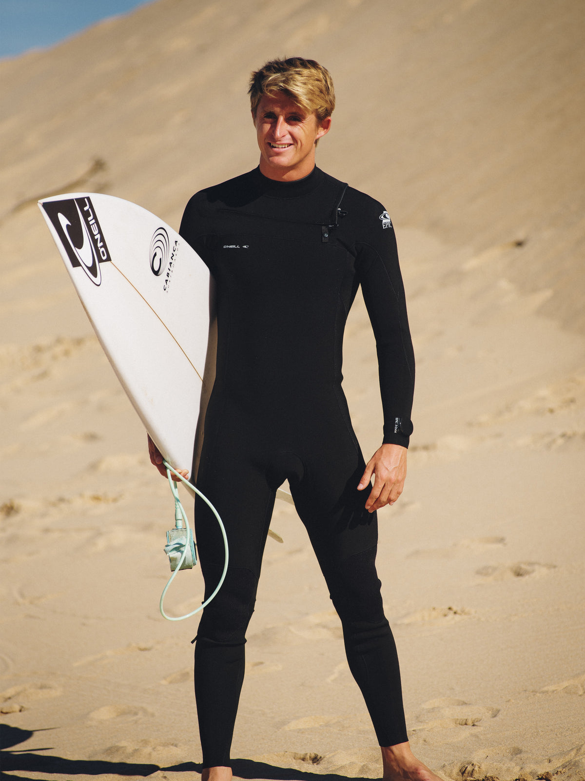 Epic 4/3mm Chest Zip Full Wetsuit Neoprenanzug für Herren, schwarz, getragen am Model am Strand von vorne
