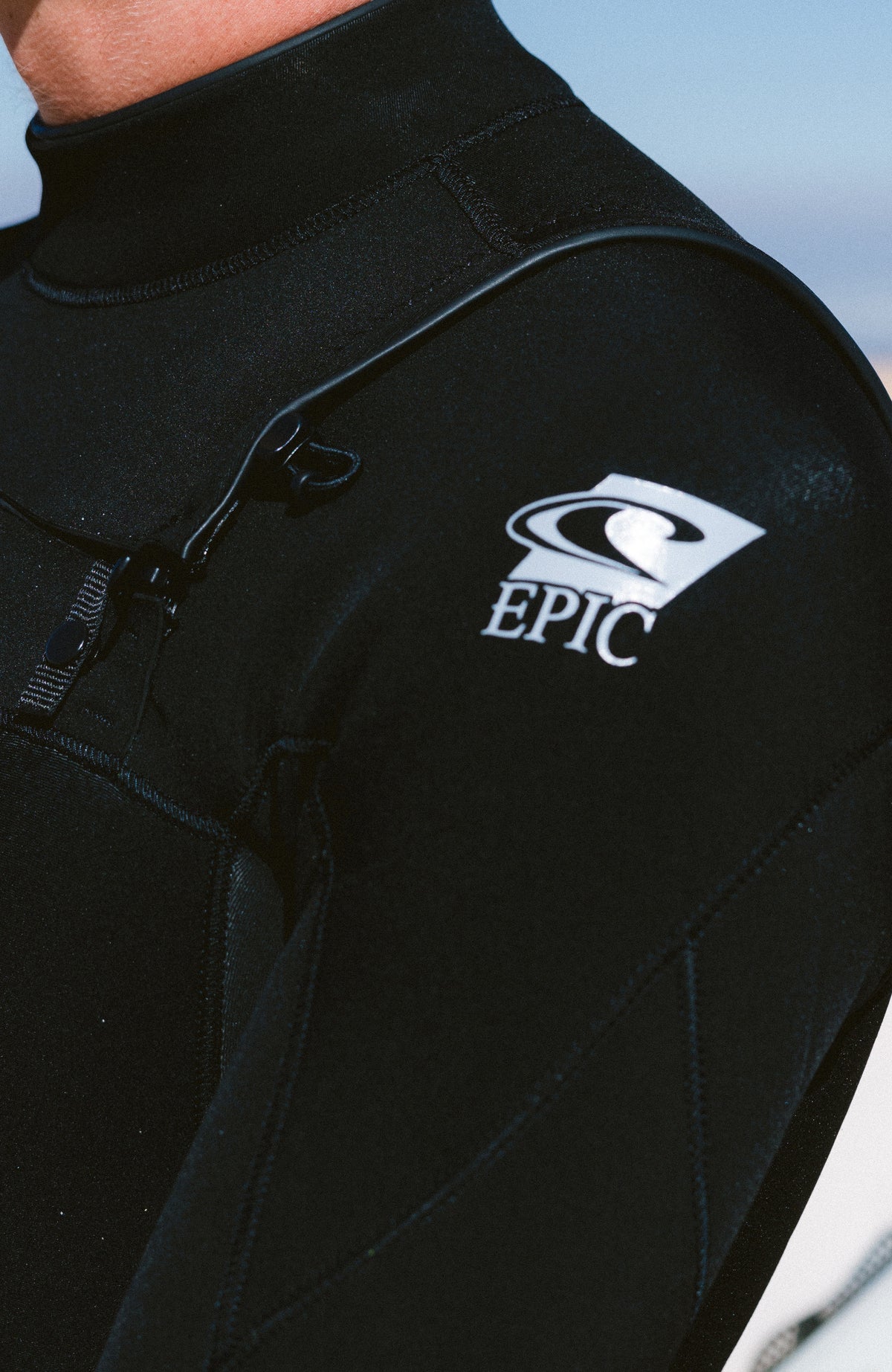 Epic 4/3mm Chest Zip Full Wetsuit Neoprenanzug, schwarz, Nahaufnahme von Front-Reißverschluss und Logo-Print am Ärmel