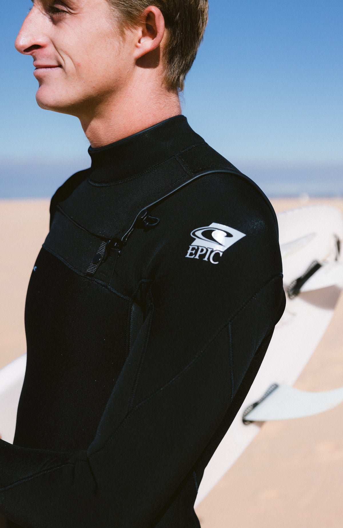 Epic 5/4mm Chest Zip Full Wetsuit Neoprenanzug, schwarz, am Strand, Nahaufnahme mit Logo-Print am Ärmel