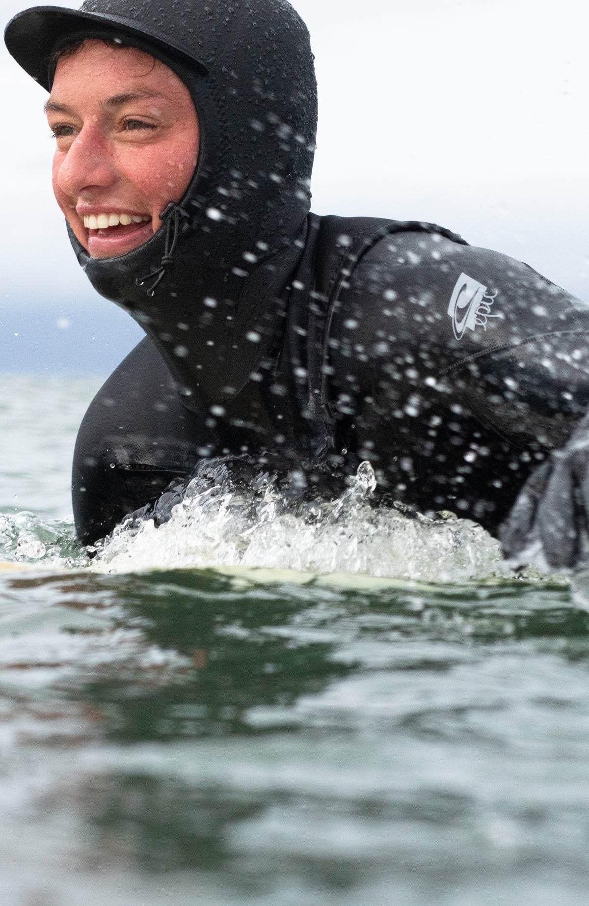 Epic 6/4 Chest Zip Wetsuit with Hood Neoprenanzug für Damen, schwarz, getragen am Model im Wasser mit Spritzwasser