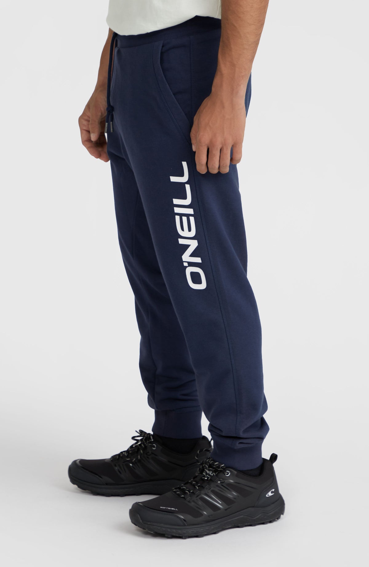 Blaue Logo Jogginghose für Herren, Seitenansicht am Model mit vertikalem Logo-Print in Weiß am Hosenbein
