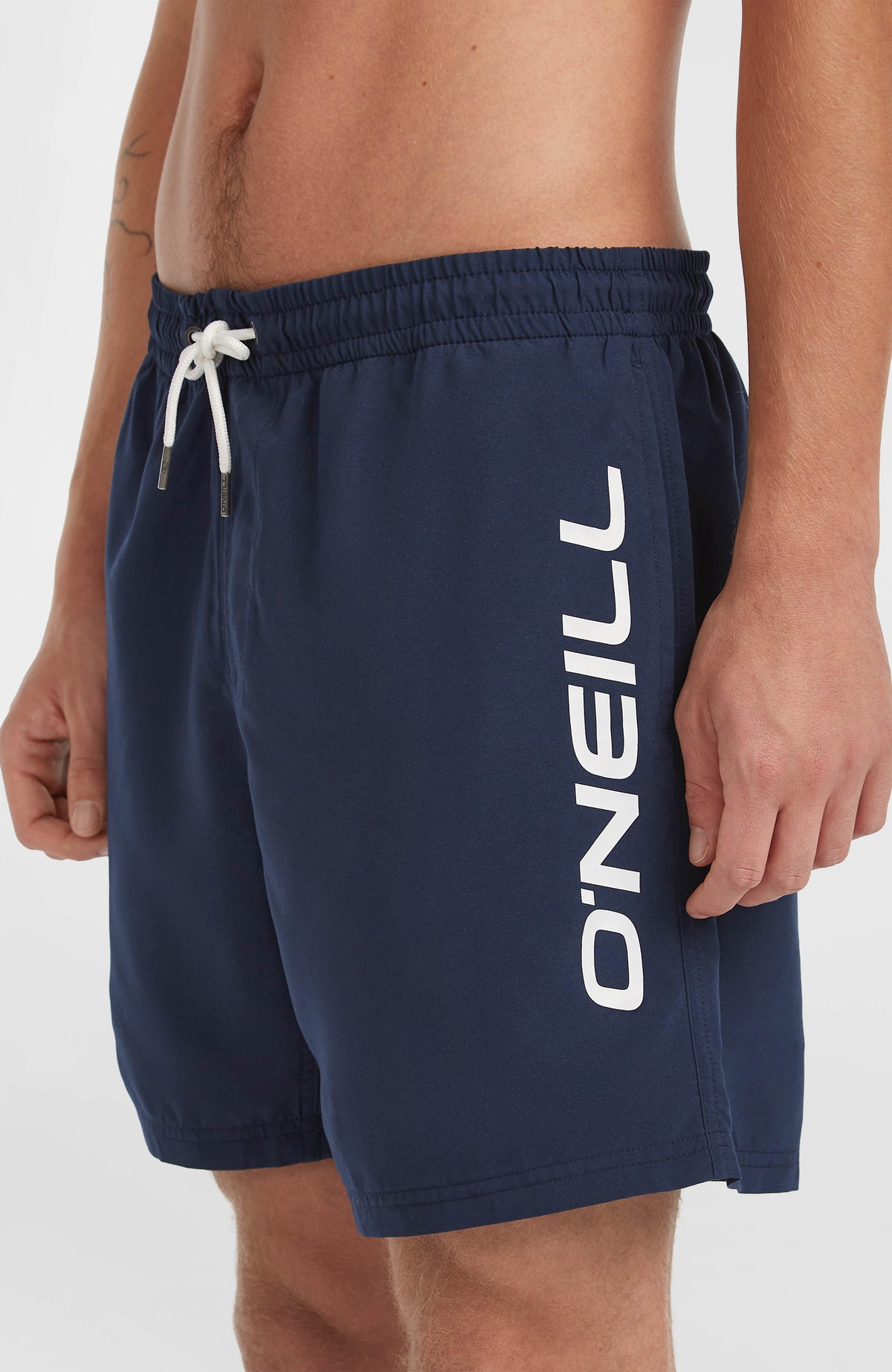 Nahaufnahme der blauen Cali 16'' Badehose am Model mit weißem Logo-Print und Kordelzug